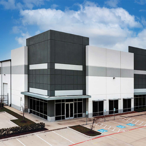 A large modern white warehouse building with dark grey accents dominates the scene and sits on a paved lot with parking areas